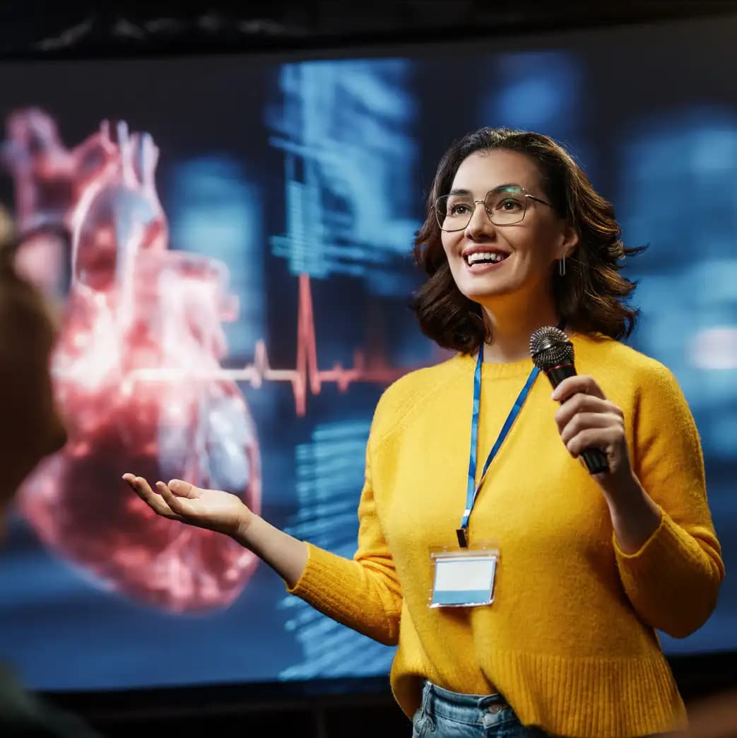 A presenter speaking to an audience in front of a large clinical display
