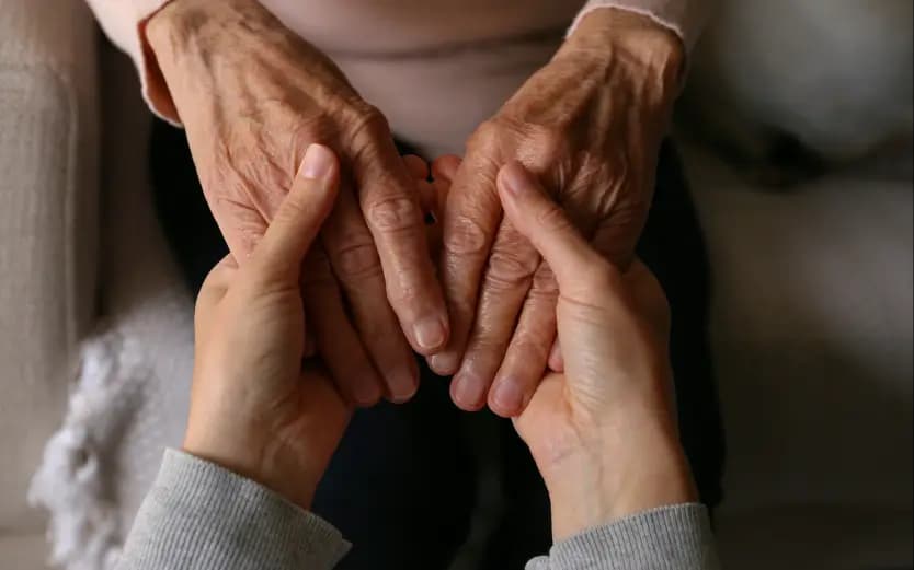 A clinician's hands supporting an older patient's hands